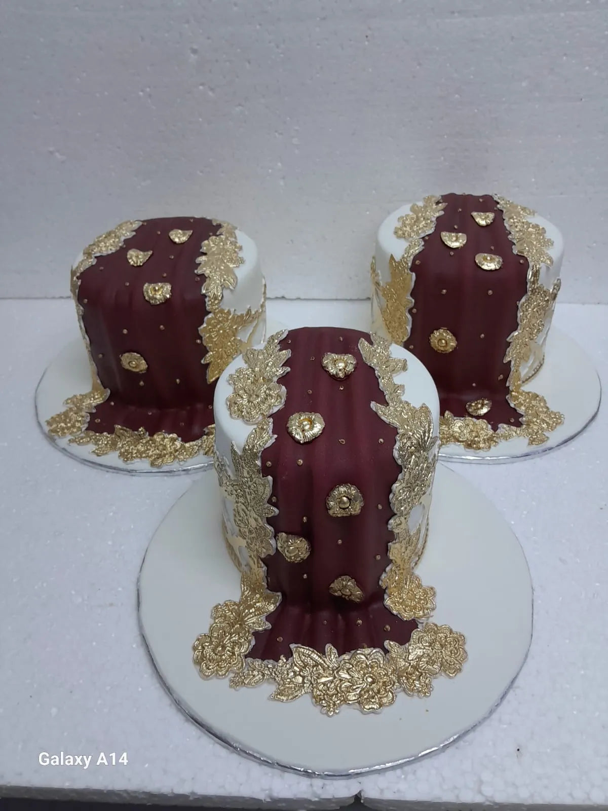 Three Wedding cakes with gold decorative elements on a white surface.