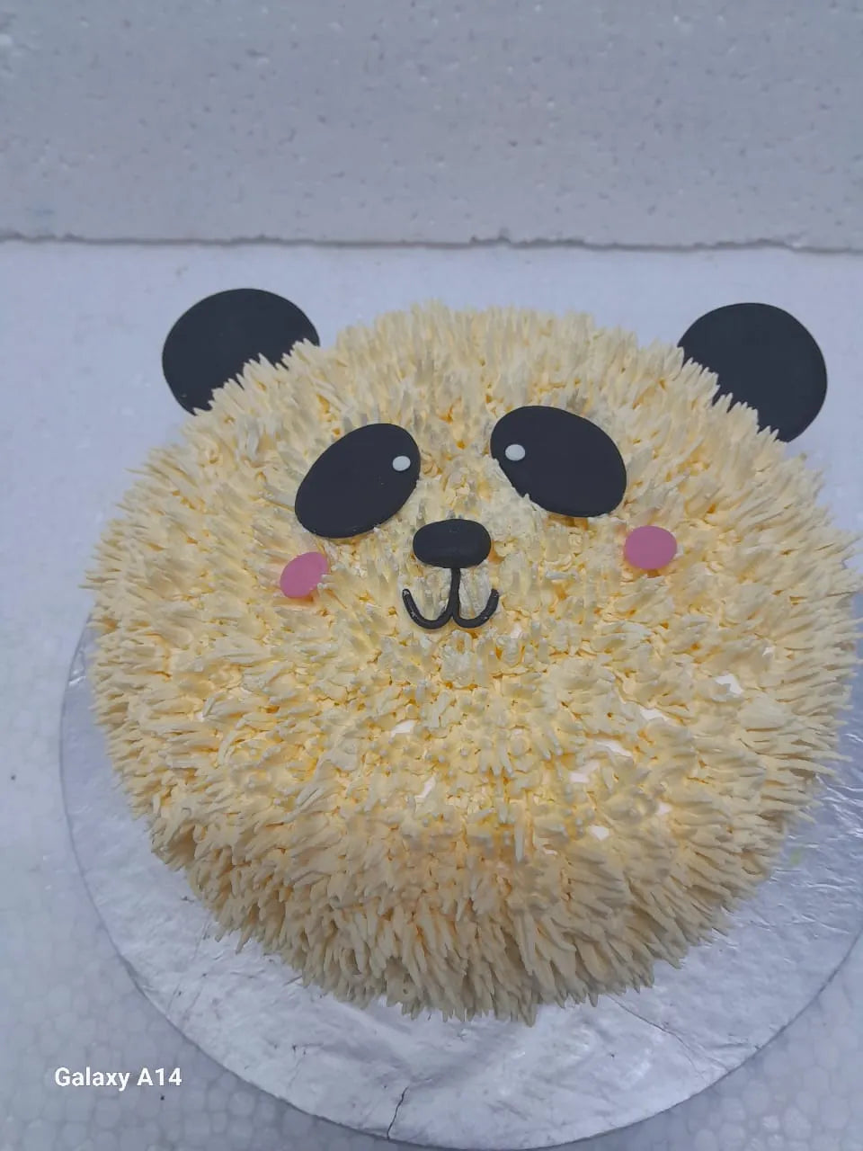 Panda-shaped cake with yellow frosting on a white background