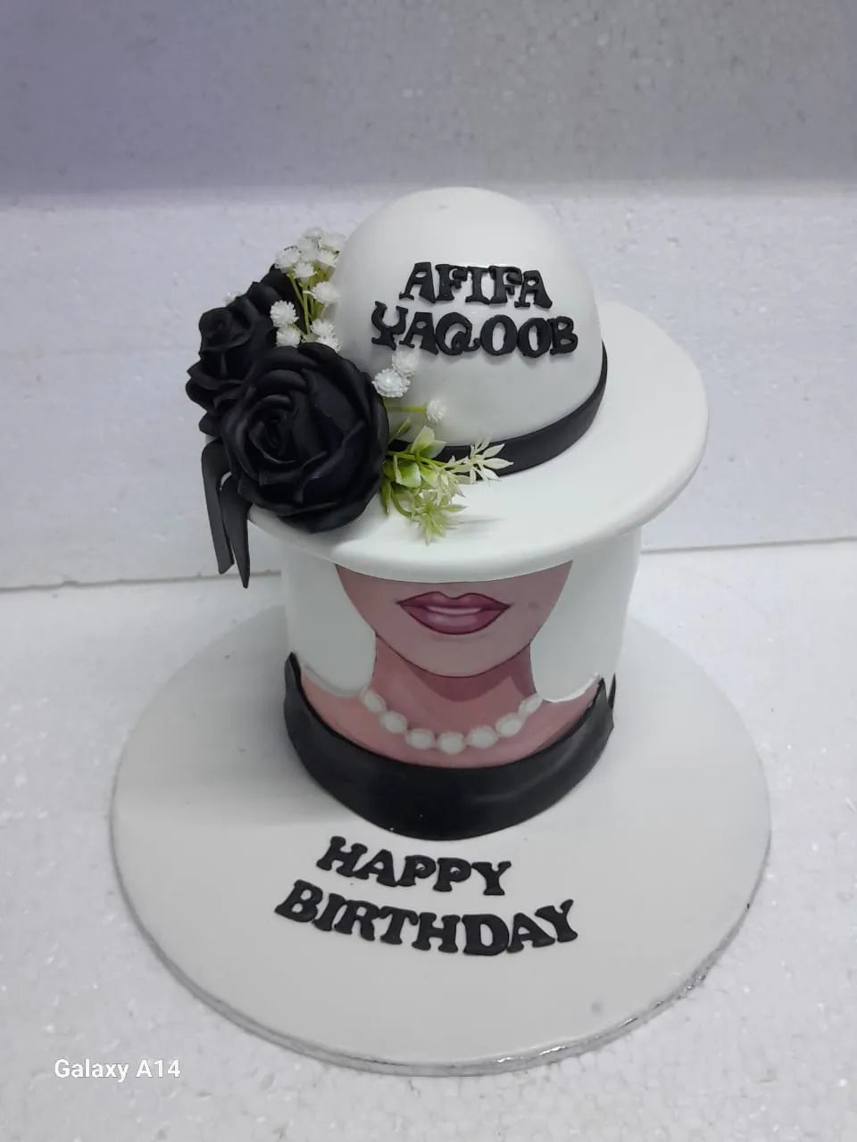 Small round cake with a white top, black rose, and 'Happy Birthday' text on a gray background