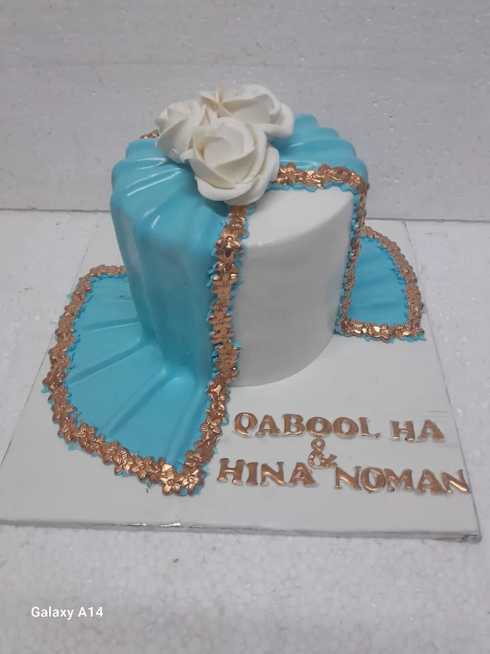 Decorative Nikkah cake with blue and white design, rose decorations, and gold accents on a white background.