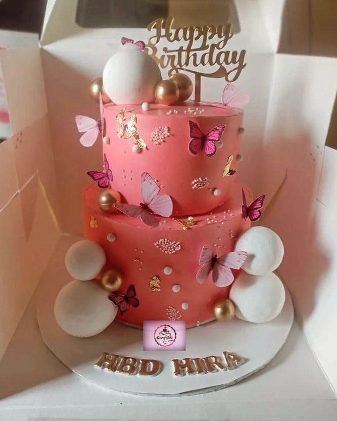 Two-tiered pink birthday cake with decorative elements on a white background