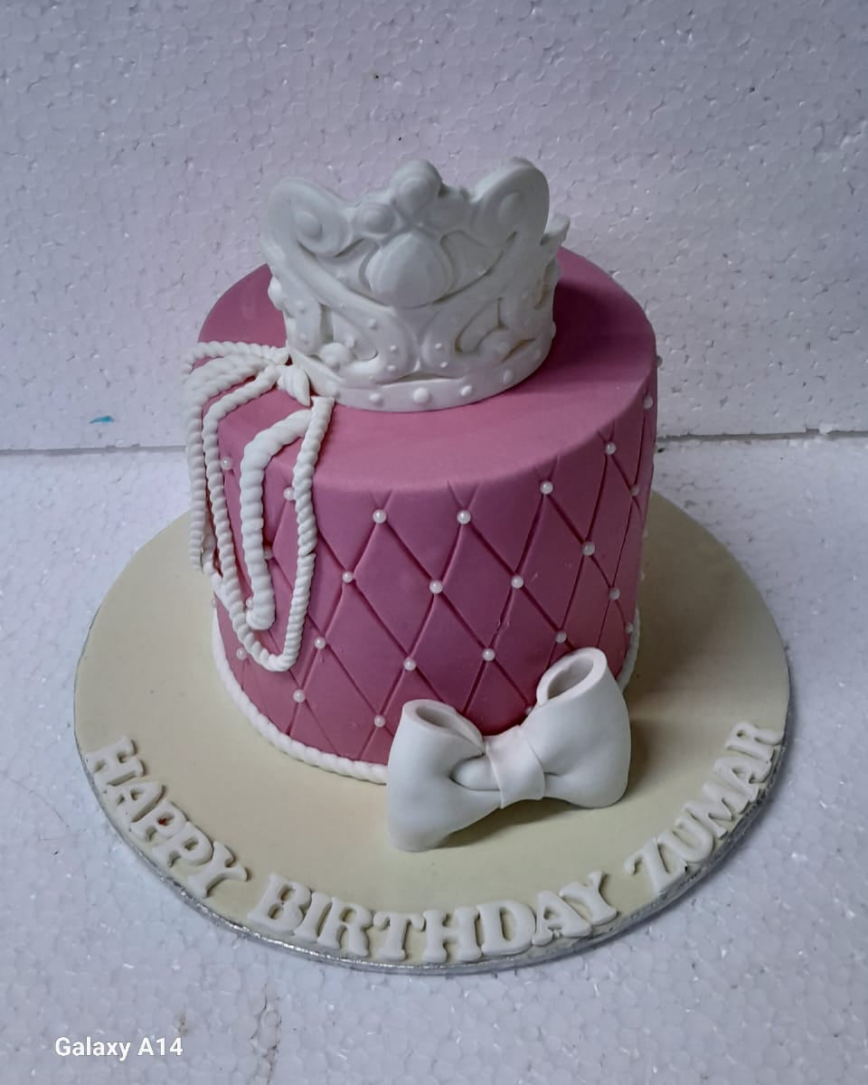 Pink birthday cake with white crown and bow on a white background