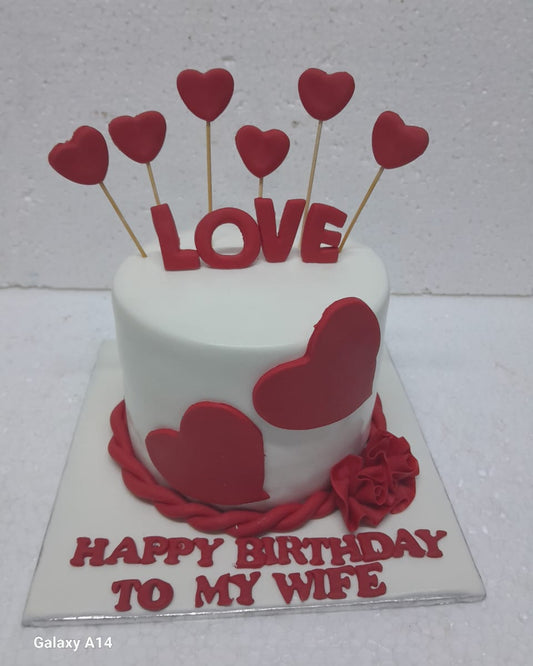 Small white cake with red hearts and 'LOVE' letters on a white background