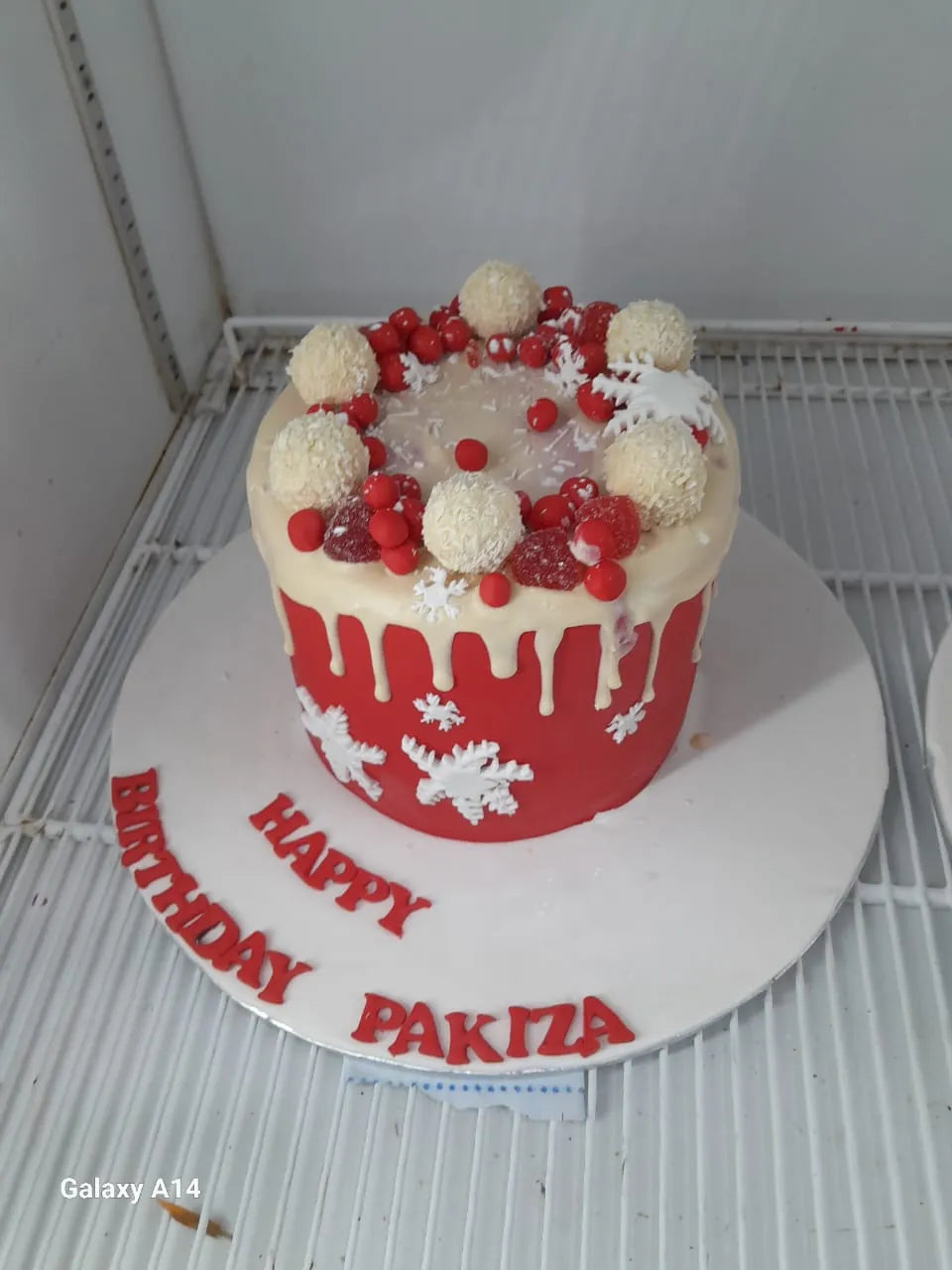 Decorative birthday cake with red and white icing on a metal rack.