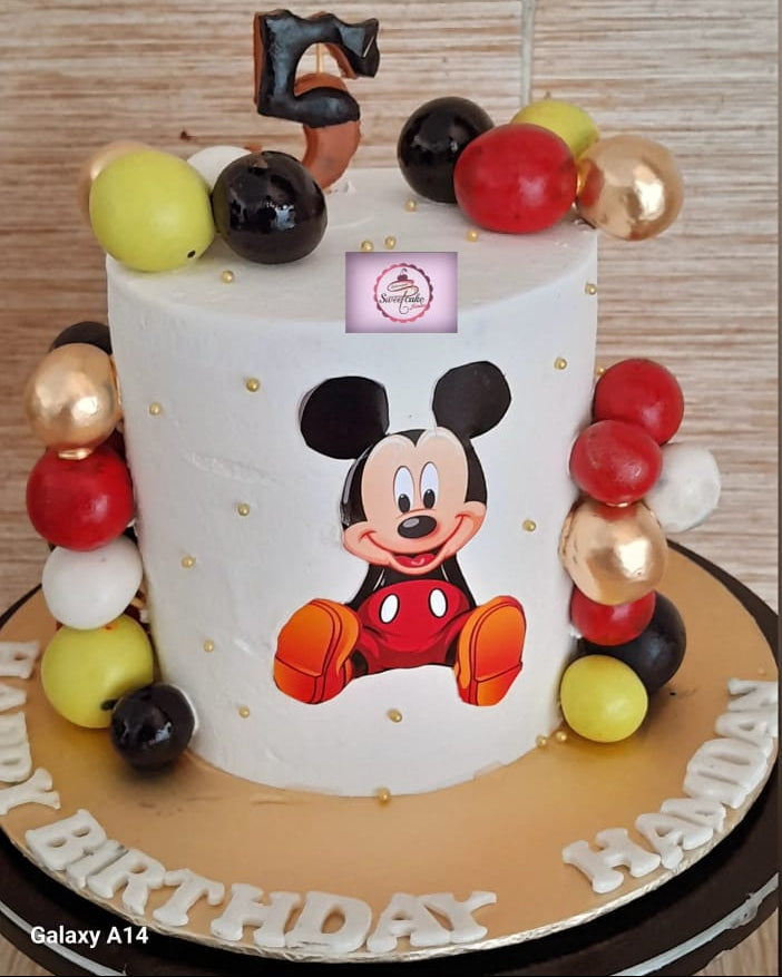 Birthday cake with Mickey Mouse design and colorful balloons on a wooden table.