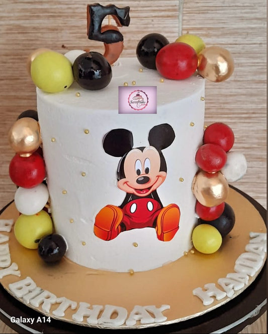 Birthday cake with Mickey Mouse design and colorful balloons on a wooden table.